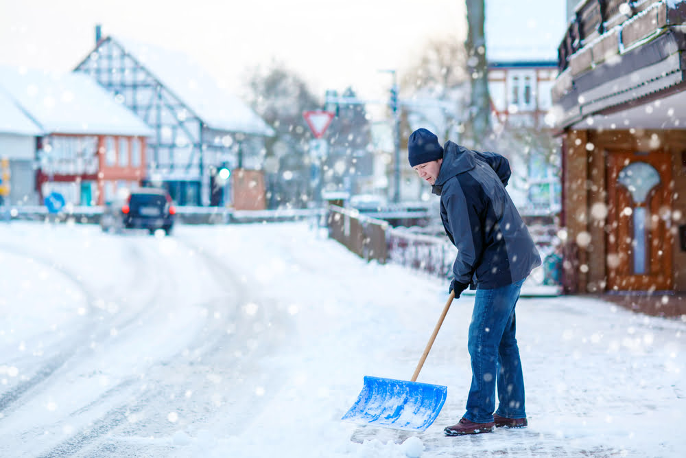 Man with snow shovel cleans sidewalks in winter